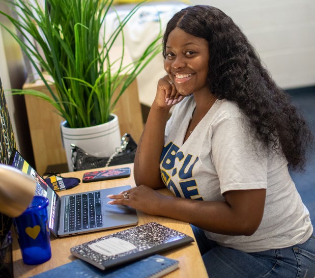 student in dorm room working on computer at desk