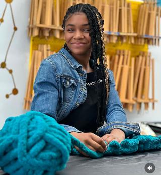 A black female knitter works with a large ball of yarn